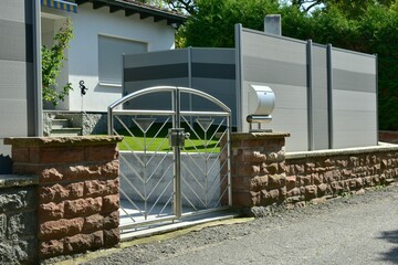 Natursteinmauer, Edelstahl-Gartentor und fest stehende Kunststoff-Sichtschutzwand und rot...