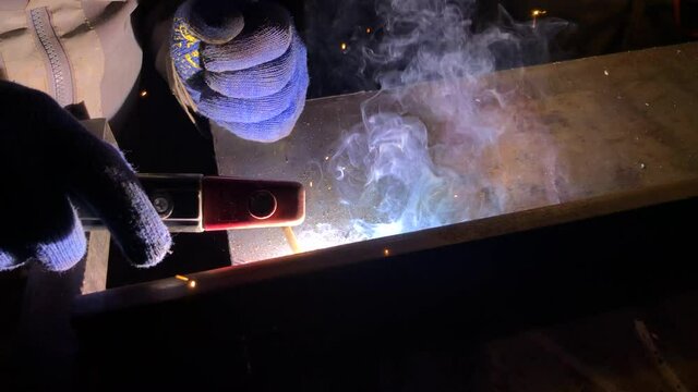Process of electric welding of metal structures. Bright flames, smoke and sparks. Master in work gloves.