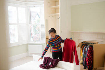 Woman unpacking clothing from moving box in bedroom