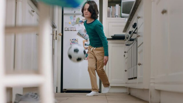 happy little boy playing with soccer ball in kitchen practicing skill having fun at home on weekend