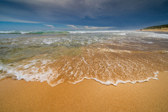 Low wide angle view of waves rolling up a golden sandy beach with dark storm clouds overhead