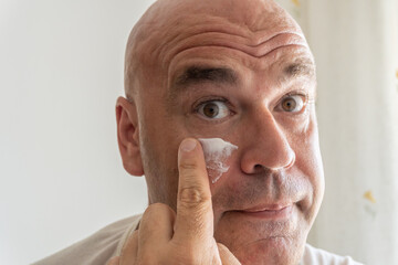 Close-up of a middle-aged Caucasian man applying facial cream to his face. 