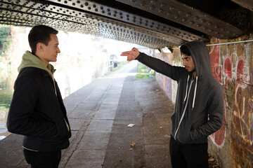 Menacing young man gesturing finger gun at man in urban tunnel