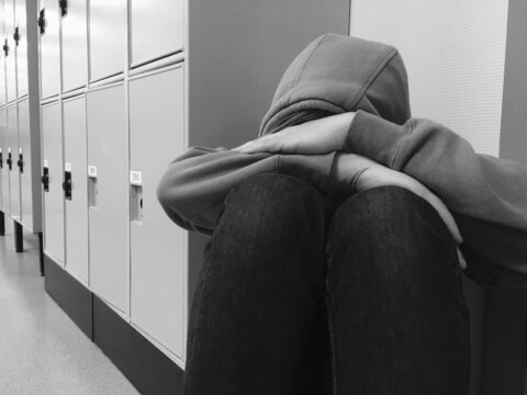 Sad person sitting in corridor in fornt of a locker in school, black and white 
