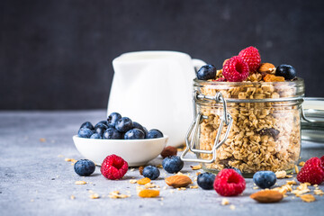 Granola with fresh berries in the glass jar. Healthy dessert or snack at stone table.
