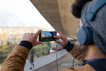 Young man with headphones using camera phone along canal