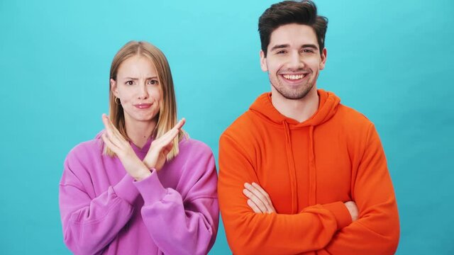 Woman show negative answer while man agree with something standing isolated over blue background in the studio