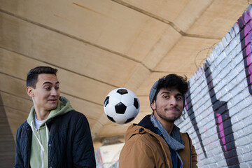 Two young men with soccer ball in urban tunnel
