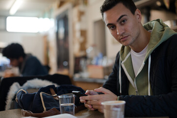 Portrait confident young male college student using smart phone in cafe