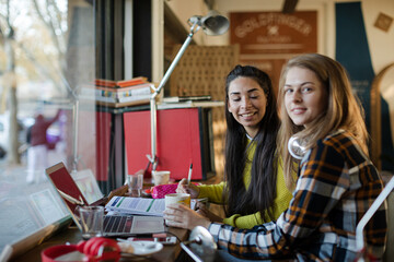 Portrait smiling female college students studying at laptop in cafe