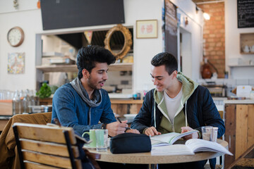 Portrait confident young male college students studying at cafe table