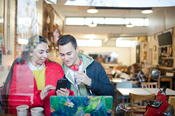 Young couple using smart phone and laptop in cafe
