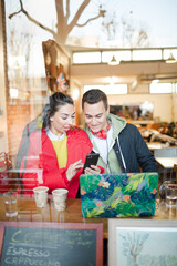 Young couple using smart phone and laptop in cafe