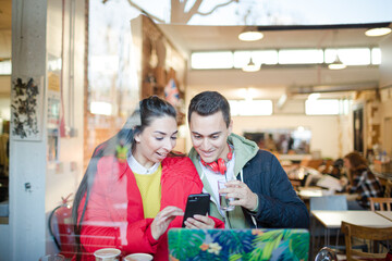 Young couple using smart phone and laptop in cafe