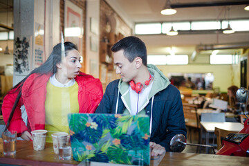 Young couple using smart phone and laptop in cafe