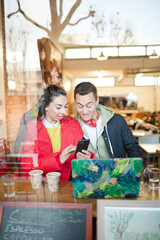 Young couple using smart phone and laptop in cafe