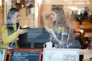 Fototapeta na wymiar Smiling female college students studying at cafe window