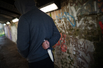 Dangerous man in hoody holding knife weapon in urban tunnel