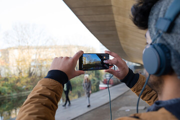 Young man with headphones using camera phone along canal