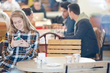 Smiling young woman using smart phone in cafe