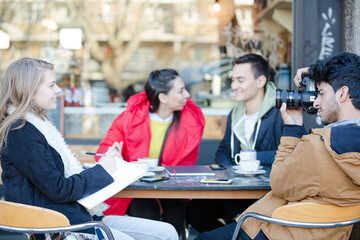 Young adult college students with digital camera at sidewalk cafe