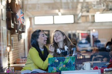 Young woman applying lip gloss to friends lips in cafe window