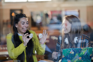Young female college students studying, eating dessert at cafe window