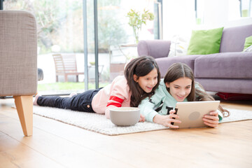 Sisters using digital tablet on living room floor