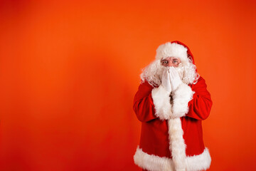 Funny cheerful santa claus points his hands to the side. A man in a Christmas costume on an orange background.
