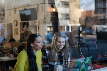 Young female college students studying at laptop in cafe window