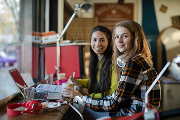 Portrait smiling female college students studying at laptop in cafe