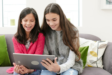 Happy sisters using digital tablet on living room sofa