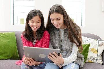Happy sisters using digital tablet on living room sofa