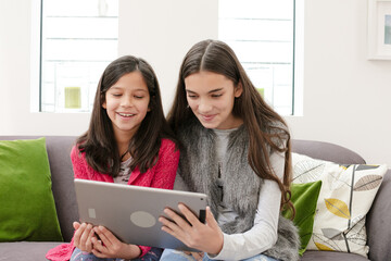 Happy sisters using digital tablet on living room sofa