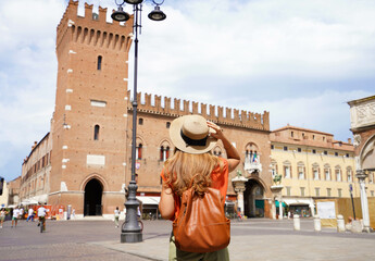 Cultural tourism in Italy. Rear view of female backpacker visiting old medieval town of Ferrara, Italy. - obrazy, fototapety, plakaty
