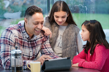 Father and daughters using digital tablet in morning kitchen