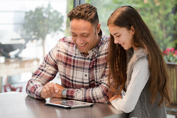 Smiling father and daughter using digital tablet at kitchen counter