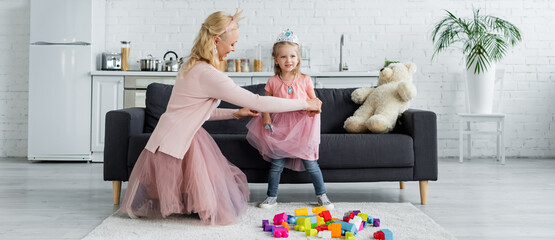 mom and kid in fairy costumes playing near building blocks on floor, banner © LIGHTFIELD STUDIOS