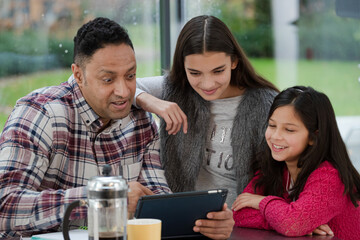Father and daughters using digital tablet in morning kitchen