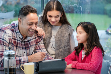 Father and daughters using digital tablet in morning kitchen