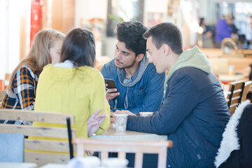 Young adult friends using smart phones at cafe table