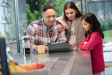 Father and daughters using digital tablet in morning kitchen