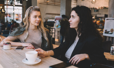 Glad women discussing plans and drinking coffee in cafeteria