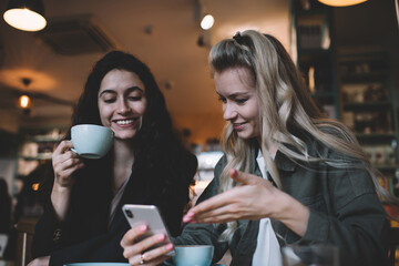 Smiling multiracial friends sitting in cafe with coffee and smartphone