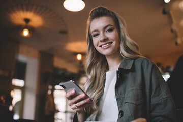 Happy young woman with mobile phone in cafeteria