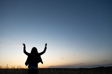 Fototapeta na wymiar silhouette of a person in sunset in field with hands raised in praise