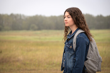 profile portrait of teen girl wearing denim jacket and backpack outdoors