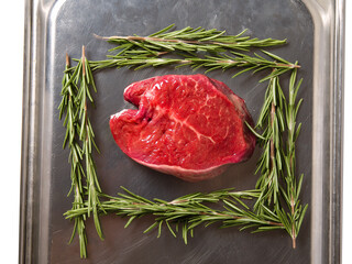 One fillet steak on a metal tray and fresh rosemary herb. Butcher craft product. Finest cut of beef. Meat industry.