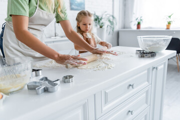 woman with daughter rolling raw dough in kitchen