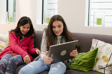 Happy sisters using digital tablet on living room sofa